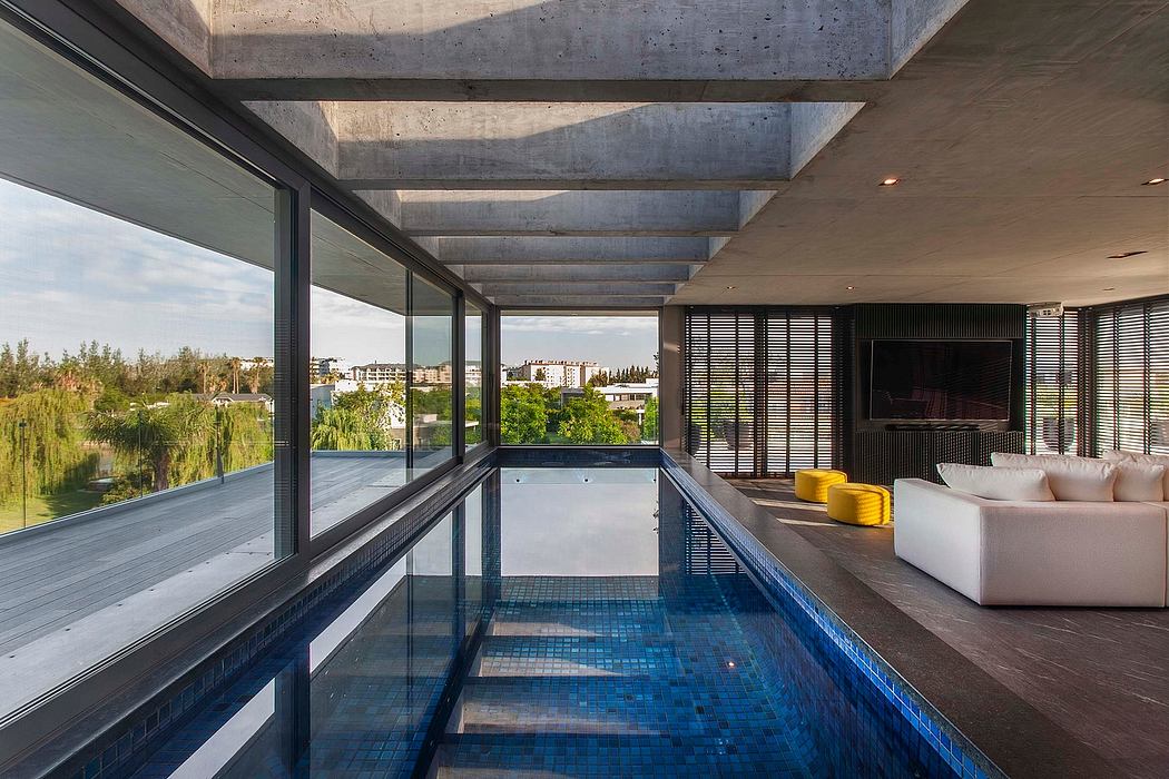 Modern open-plan interior with concrete ceiling beams, glass walls, and indoor pool.