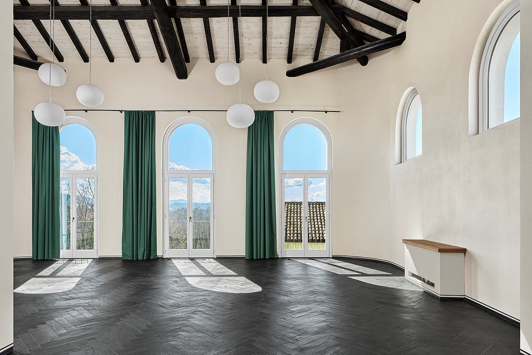 Spacious room with arched windows, dark wooden ceiling beams, and ornate light fixtures.