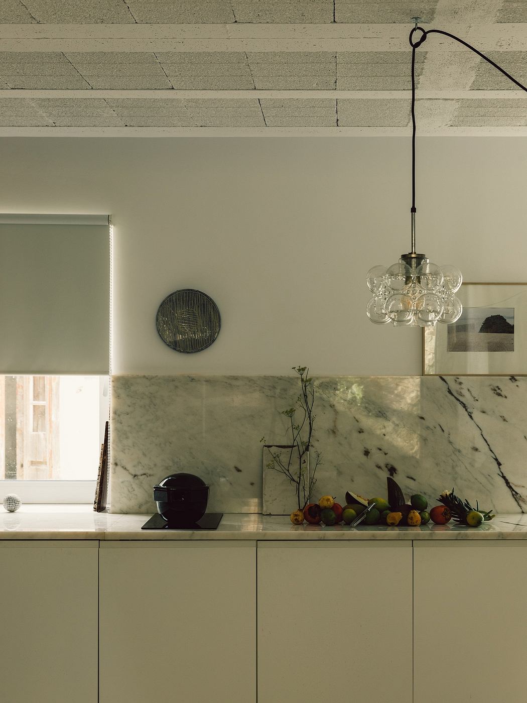A modern kitchen with a marble countertop, minimal cabinetry, and a hanging glass chandelier.