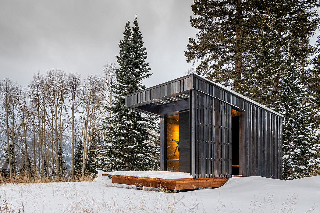 A modern, minimalist cabin with warm lighting and a wooden deck, surrounded by snowy pines.