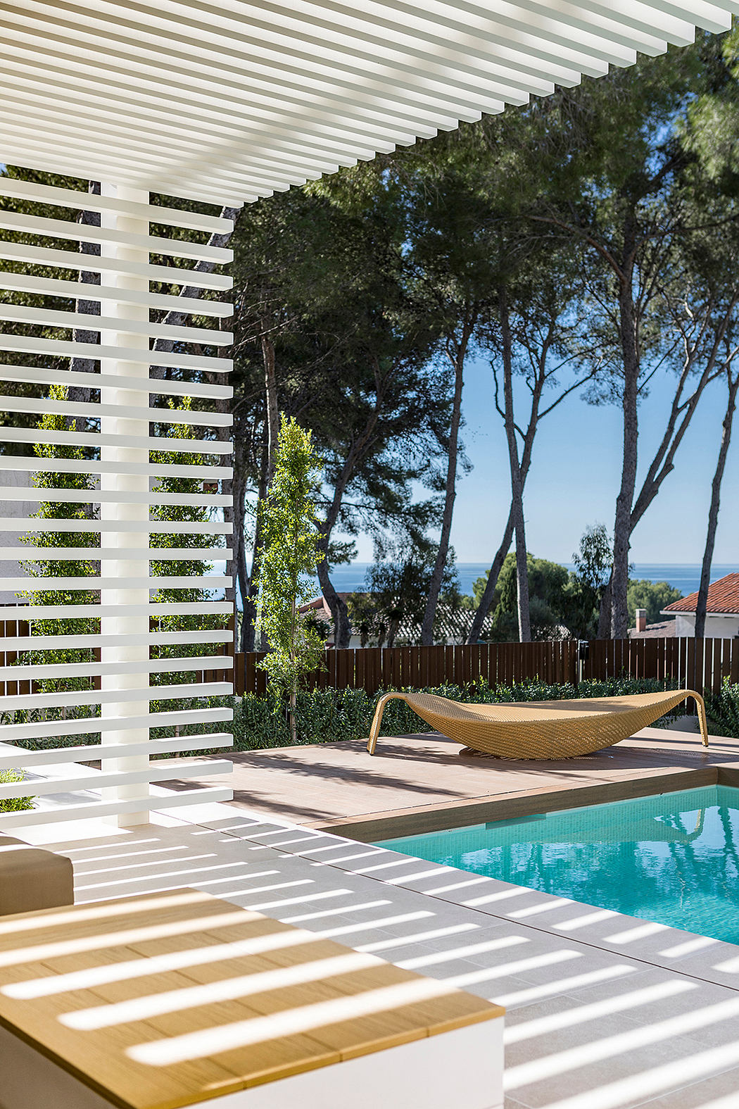 Sleek outdoor pavilion with wooden lounge, pool, and lush greenery framing the view.