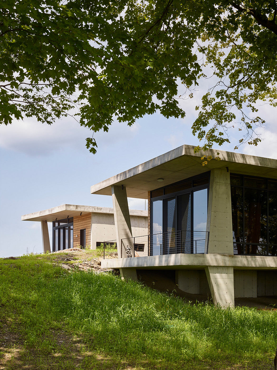 Modern concrete and wooden structure surrounded by lush greenery on a hillside.