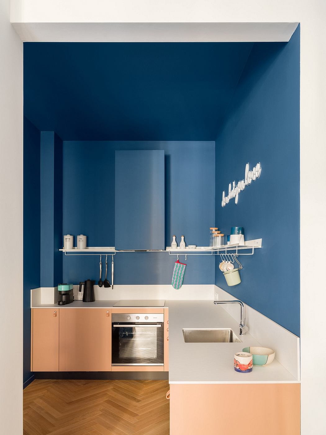 Vibrant blue kitchen with minimalist design, floating shelves, and herringbone flooring.