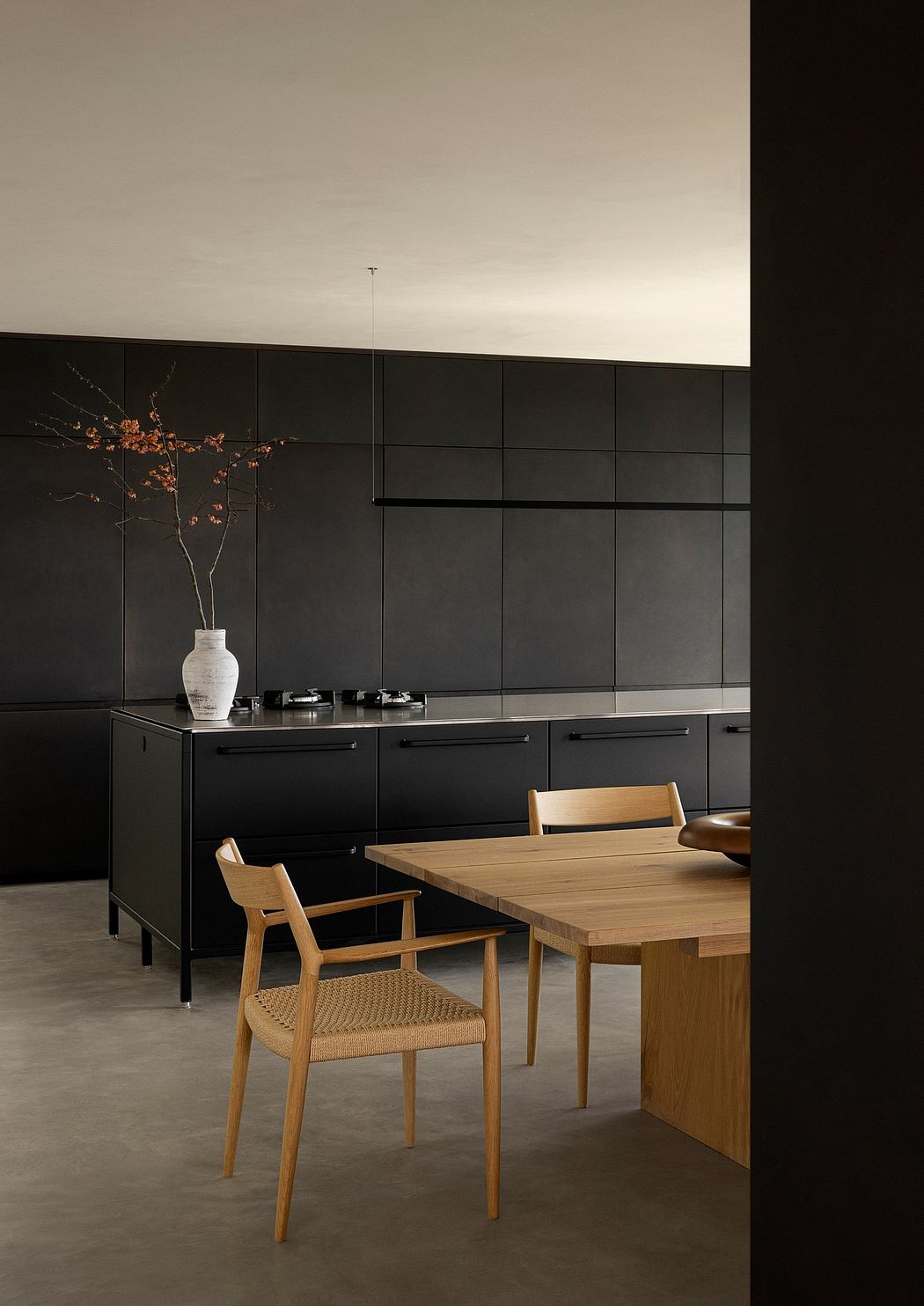 A modern, minimalist dining area with a wooden table, chairs, and black cabinetry.