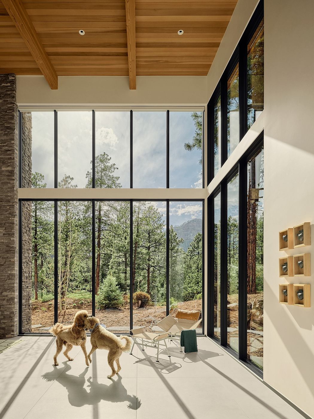 Modern mountain home with expansive glass walls, wooden ceiling, and stone accents.