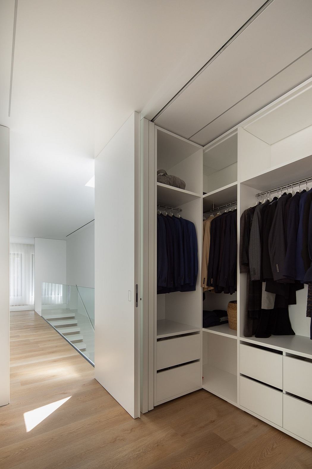 A spacious modern closet with sleek white cabinets, hanging rods, and wooden floors.