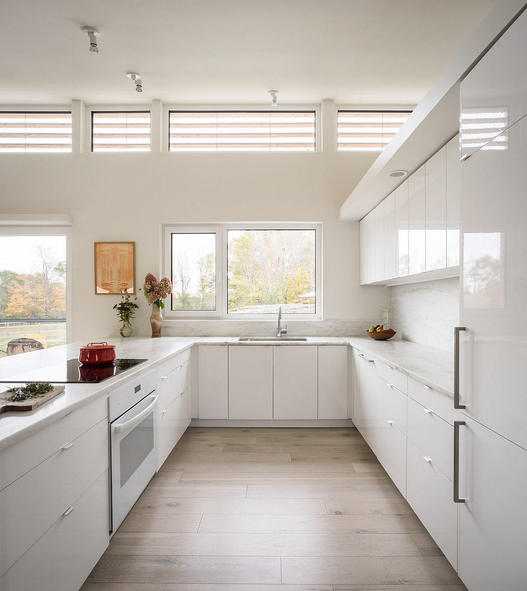 Modern U-shaped kitchen with white cabinetry, large windows, and hardwood floors.