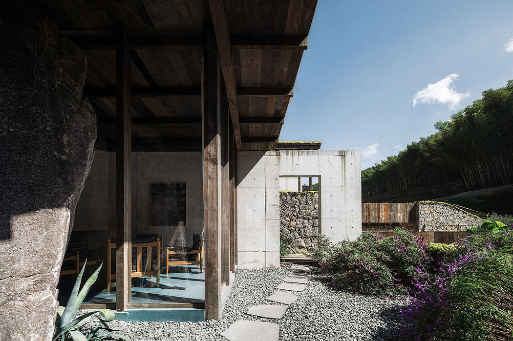 A modern, minimalist structure with concrete walls and wooden beams, surrounded by lush greenery.