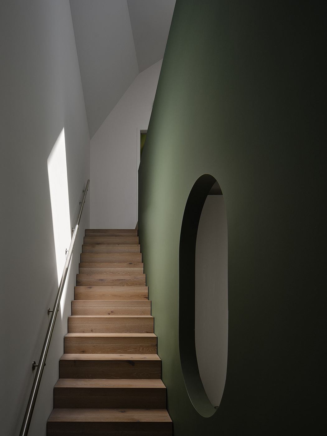 Minimalist staircase with wooden steps and a curved, green-accented wall niche.