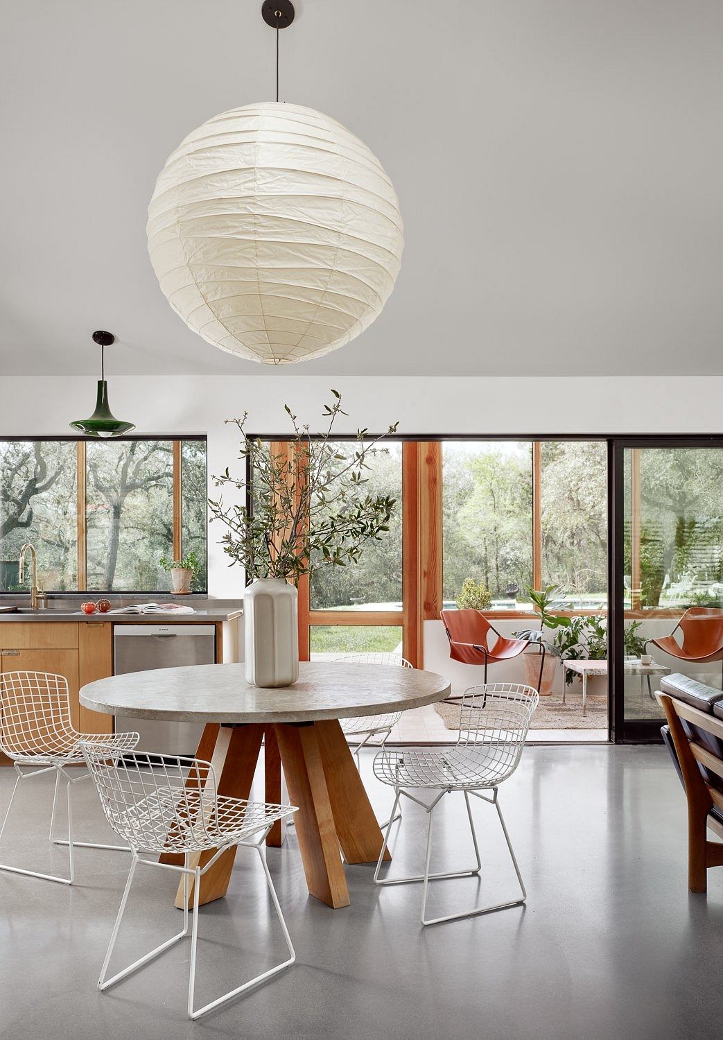 A modern, open-concept kitchen with a round marble table, wire chairs, and a large paper lantern overhead.