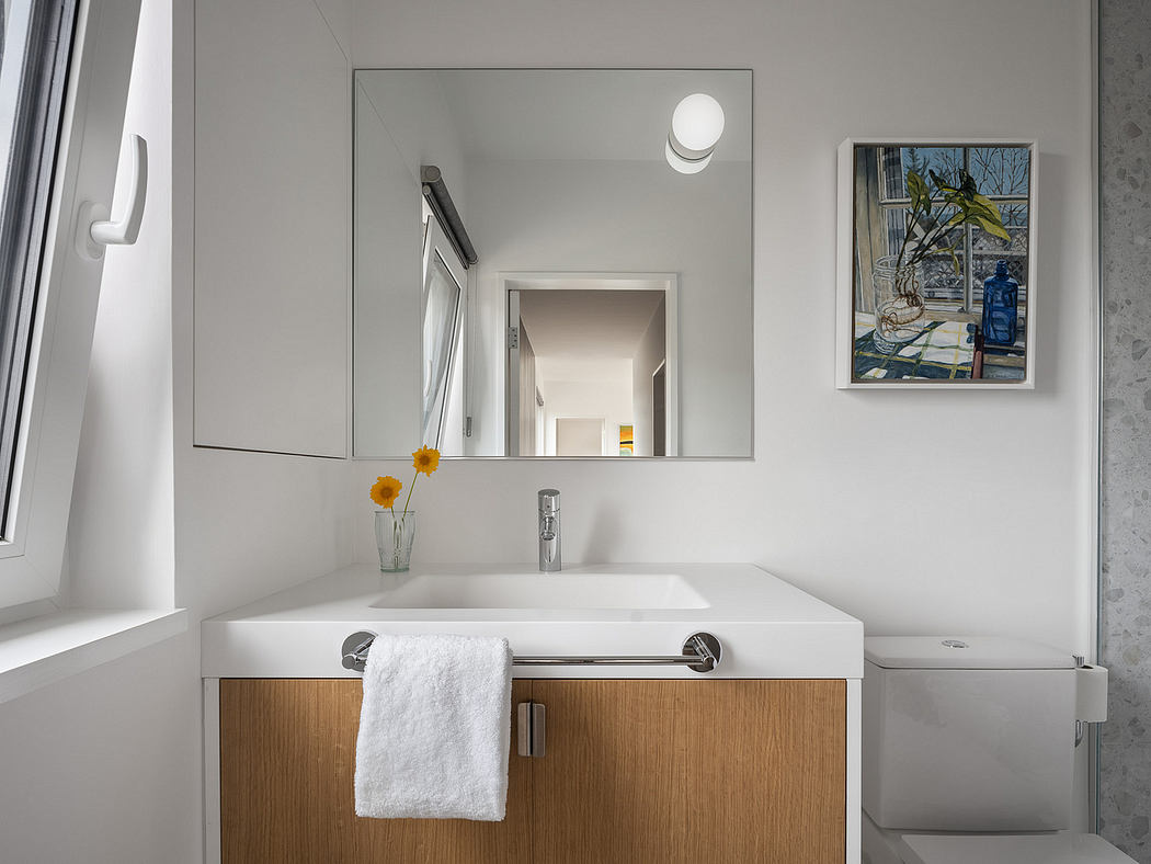 Modern, minimalist bathroom with white walls, wooden vanity, and framed artwork.