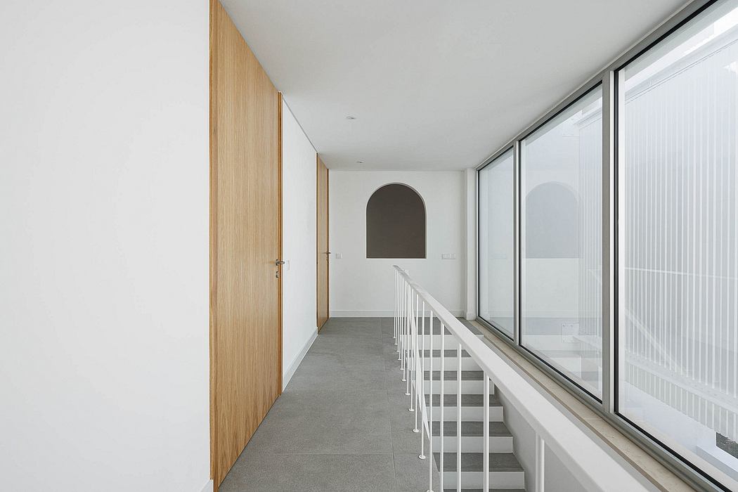 Sleek, minimalist hallway with wooden doors, floor-to-ceiling windows, and a curved archway.