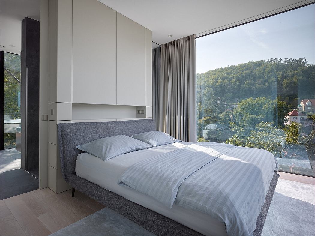 Minimalist bedroom with large window offering panoramic forest views and contemporary furnishings.