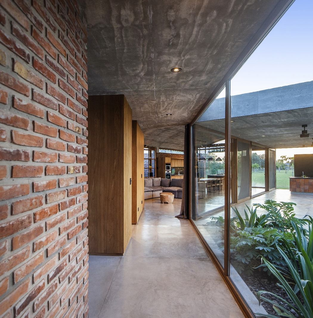 Hallway with exposed concrete ceiling, brick walls, and large glass windows overlooking a garden.