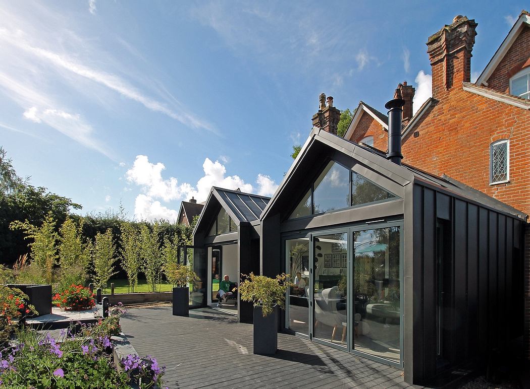 A modern, glass-enclosed architectural addition to a historic brick building, surrounded by lush greenery.