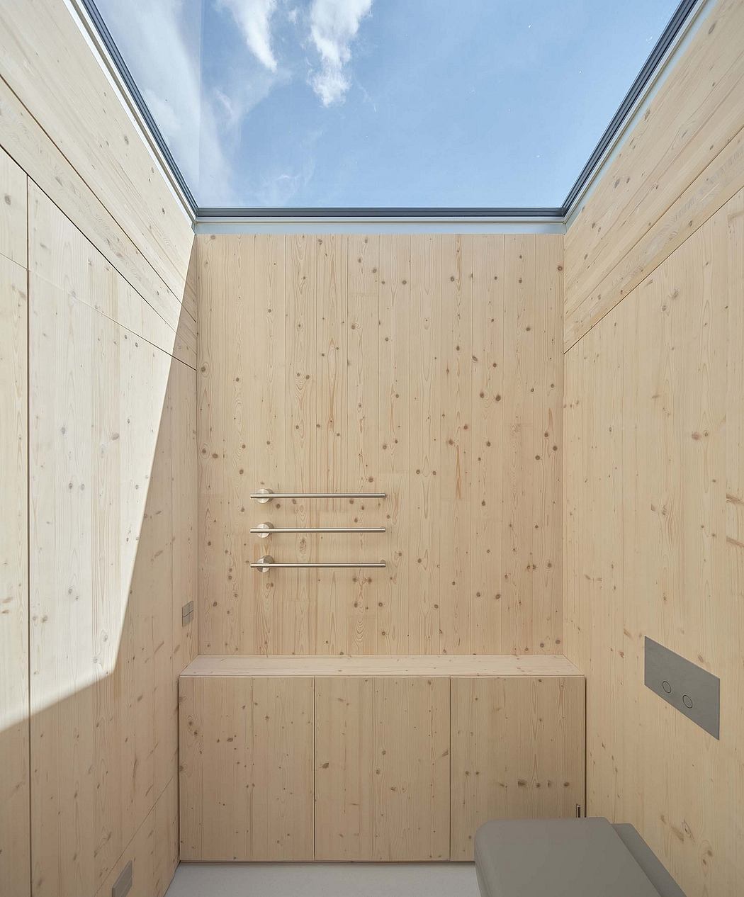 A wood-paneled room with a large skylight, built-in cabinets, and a minimalist towel rack.