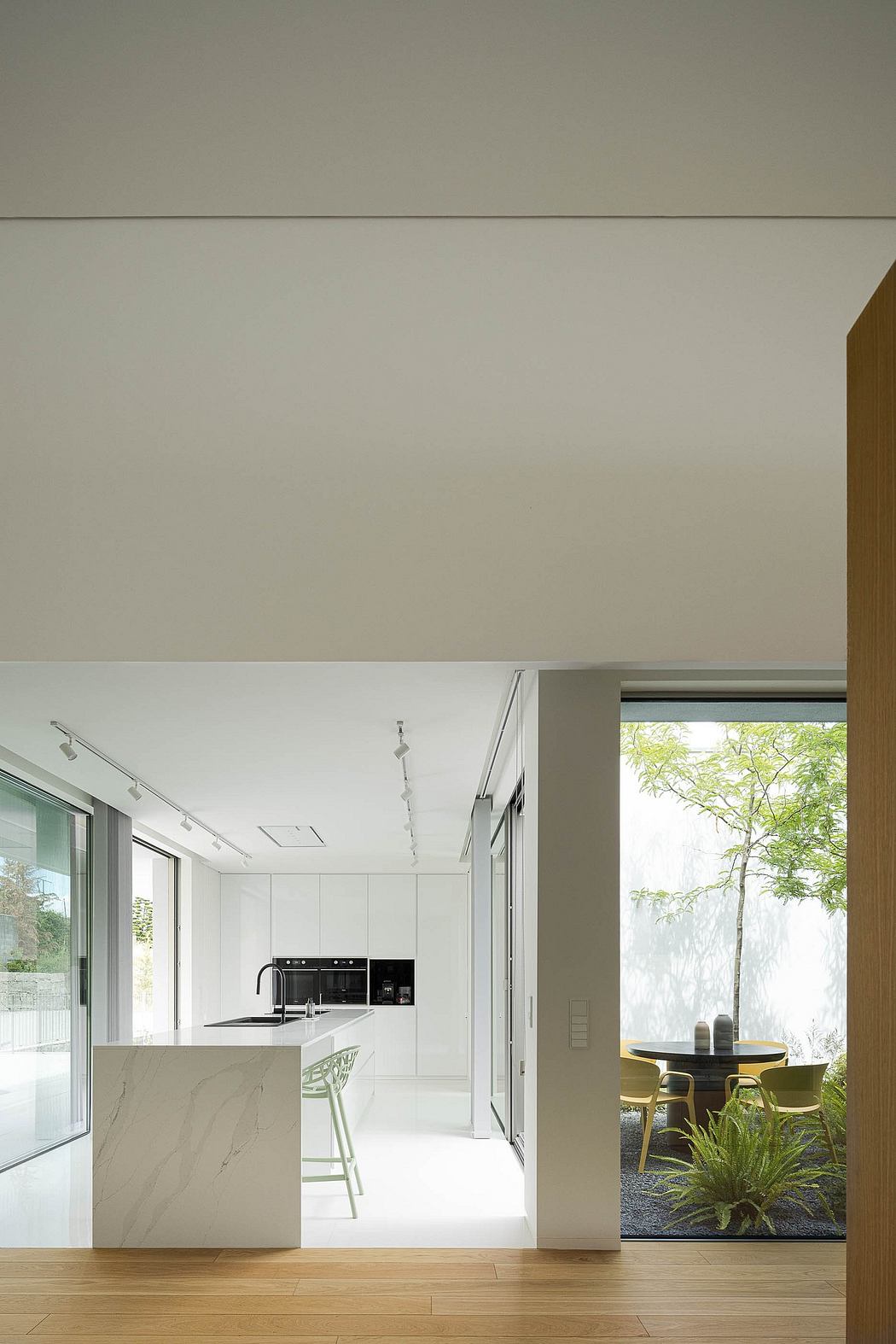 Minimalist kitchen with marble countertop, pendant lighting, and garden view through glass doors.