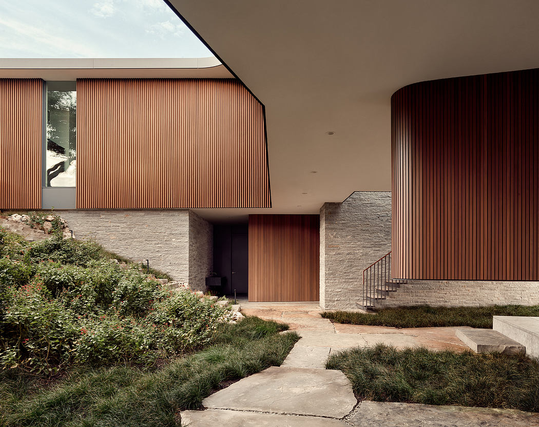 A modern, wooden-clad entryway leads to a stone-lined interior through verdant landscaping.