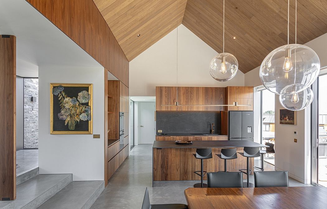 Modern open-plan kitchen and dining area with wooden walls, suspended lighting, and artwork.