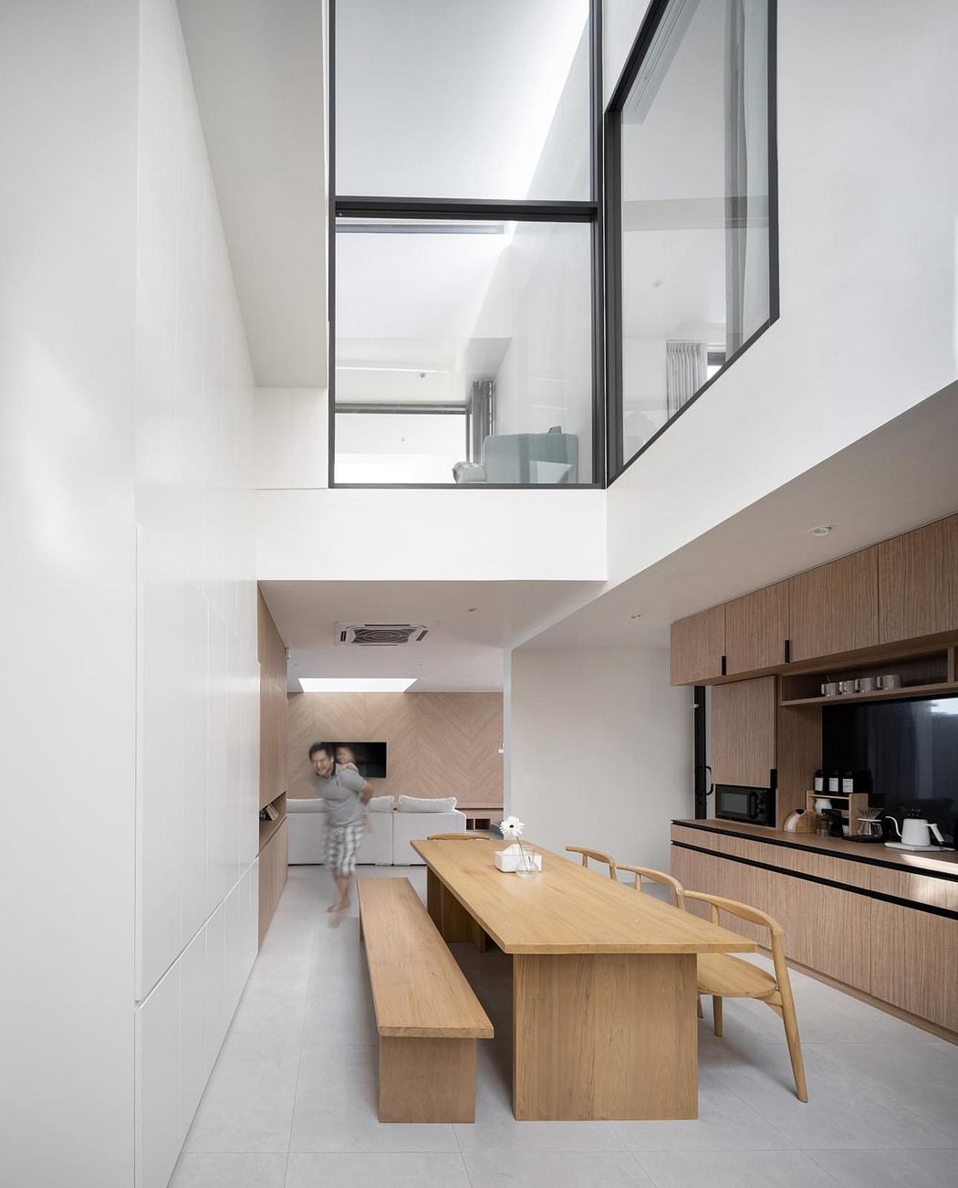 Spacious modern kitchen with wood cabinetry, long dining table, and floor-to-ceiling windows.