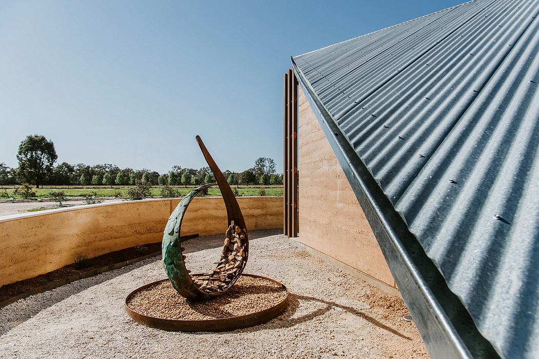 A modern architectural structure with a curved metal roof and a sculptural metal artwork in the foreground.
