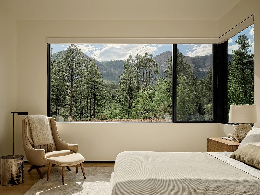 Spacious bedroom with expansive windows showcasing lush forest scenery and mountains.