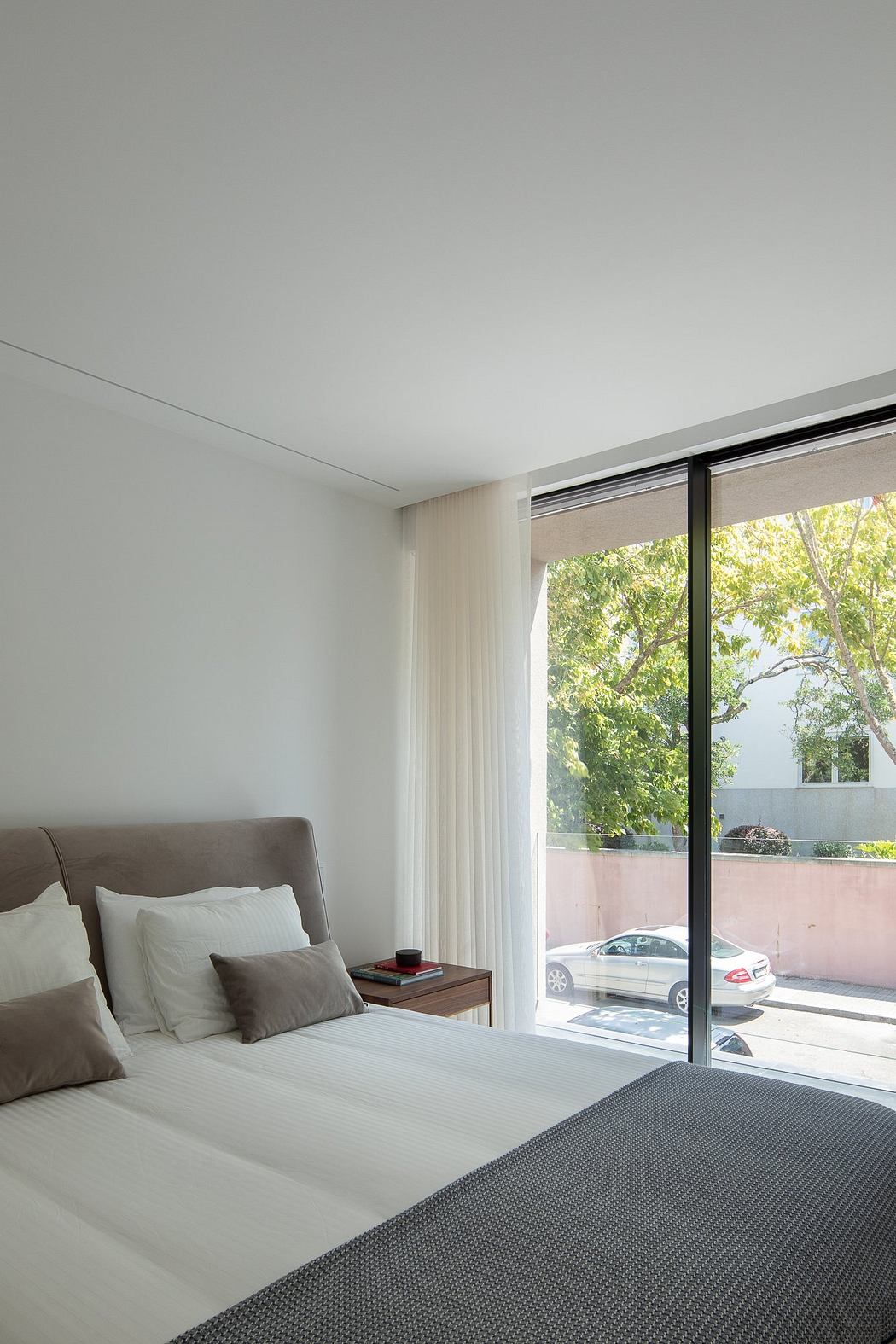 Minimalist bedroom with floor-to-ceiling windows overlooking a lush green landscape.