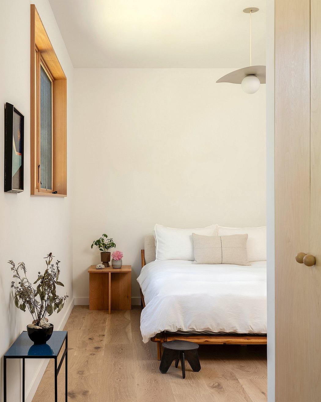 Minimalist bedroom with wooden accents, potted plant, and pendant light fixture.