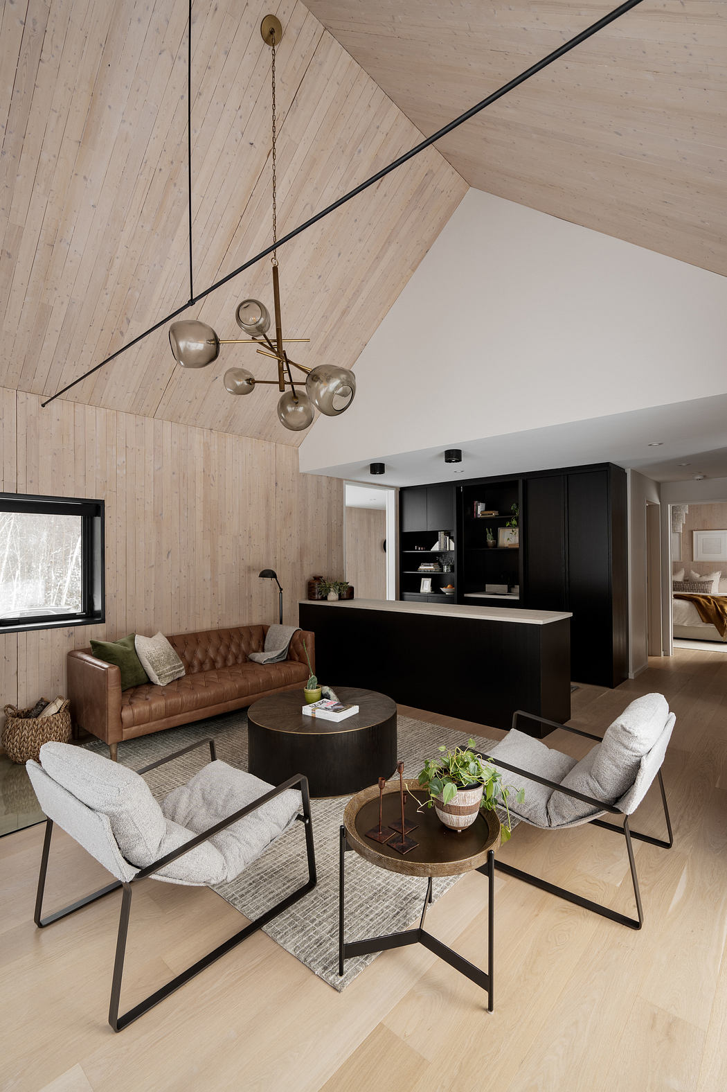Rustic wood-paneled ceiling with modern hanging light fixture, leather sofa, and minimalist furniture.
