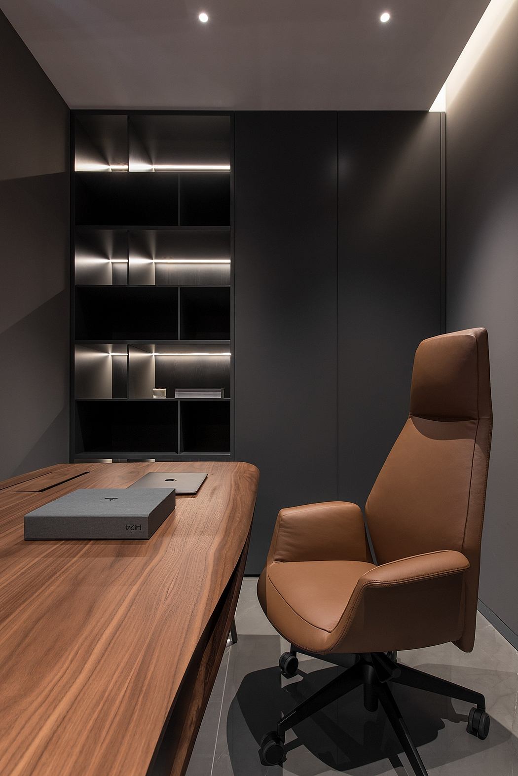 A modern, minimalist home office with a sleek wooden desk, leather chair, and recessed shelving.