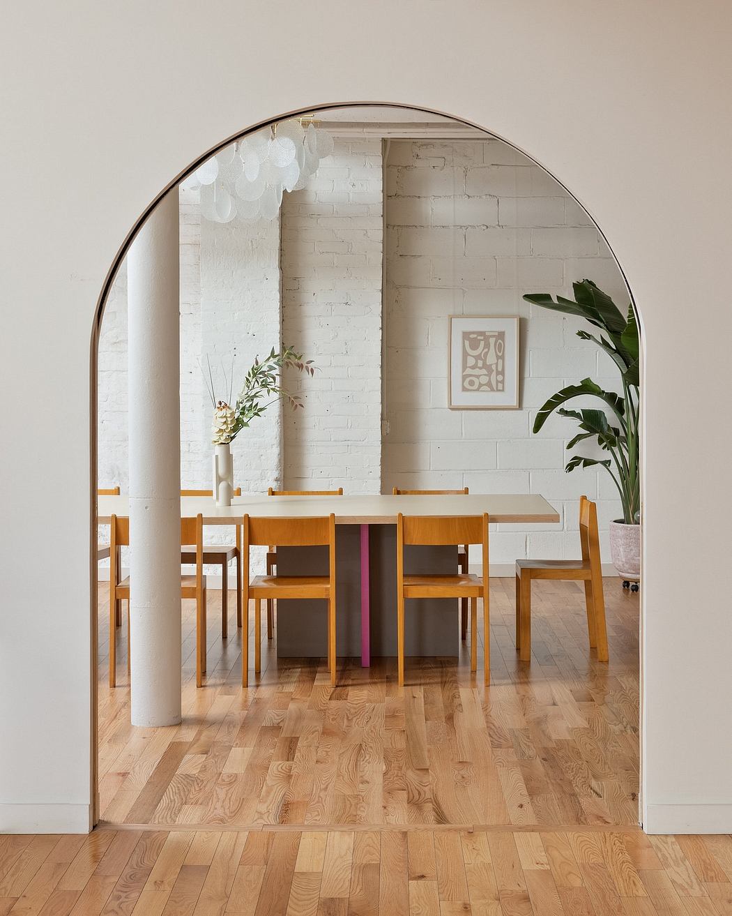 Stylish dining area with wooden table and chairs, framed by arched mirror, white brick wall.