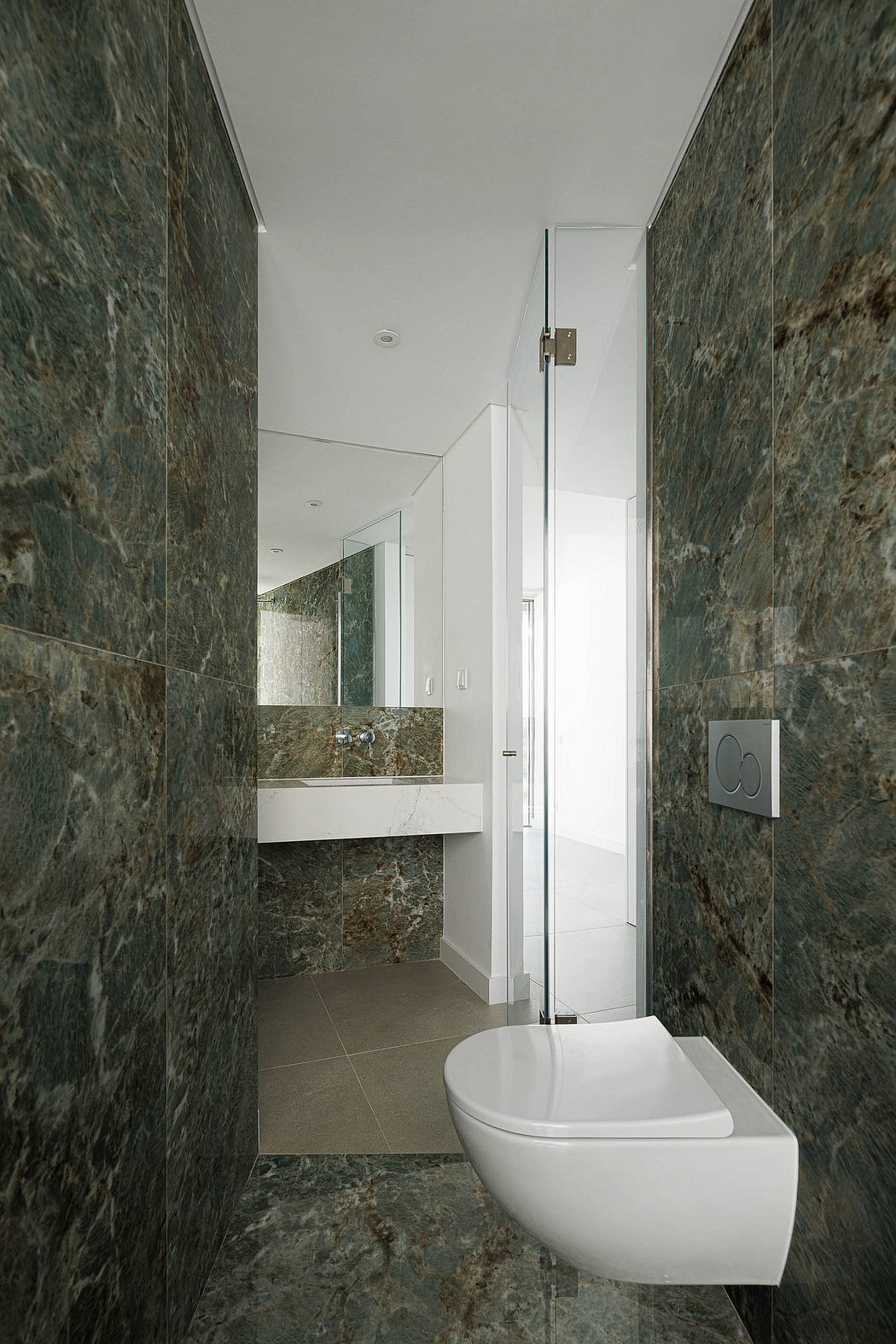 Sleek modern bathroom with bold green marble walls, minimalist vanity, and corner toilet.