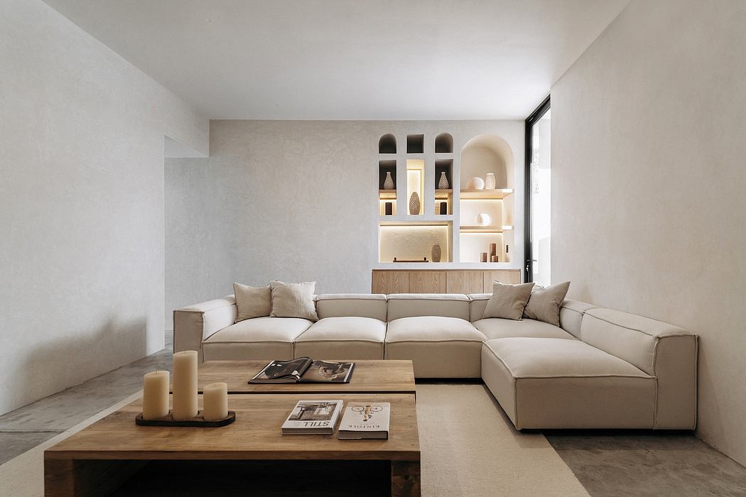 Minimalist living room with a large sectional sofa, wooden coffee table, and shelving with decorative items.