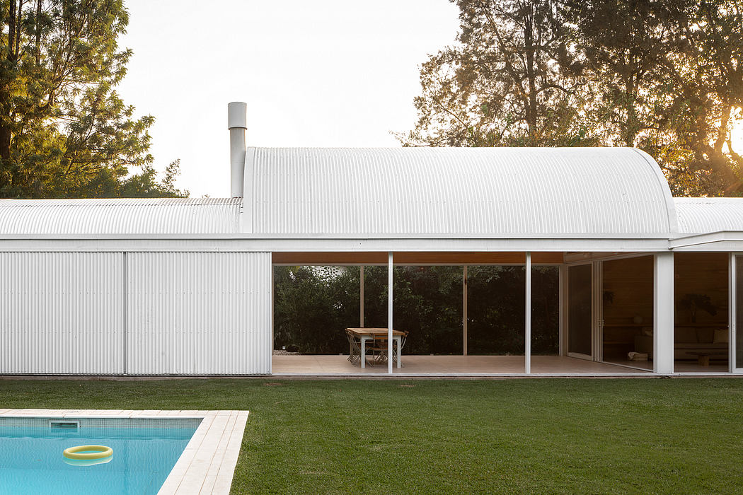 A modern, single-story home with a curved, corrugated metal roof and large windows overlooking a swimming pool.