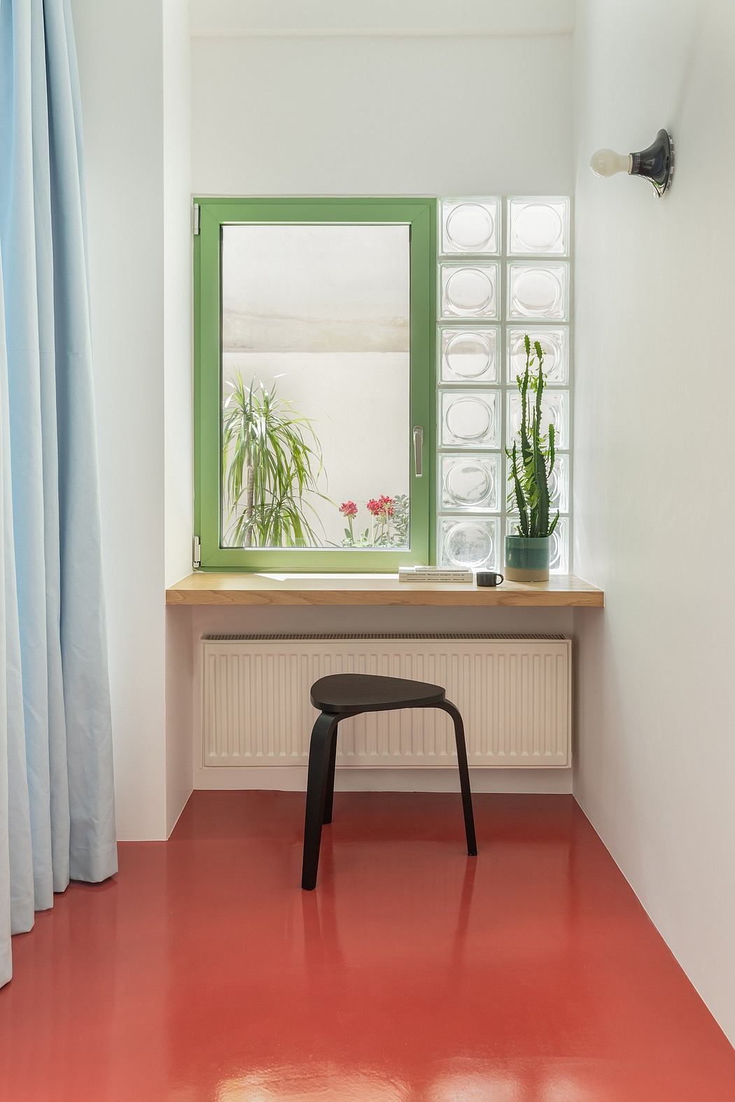 A modern, minimalist interior with a vibrant red floor, textured walls, and a wood-topped console.
