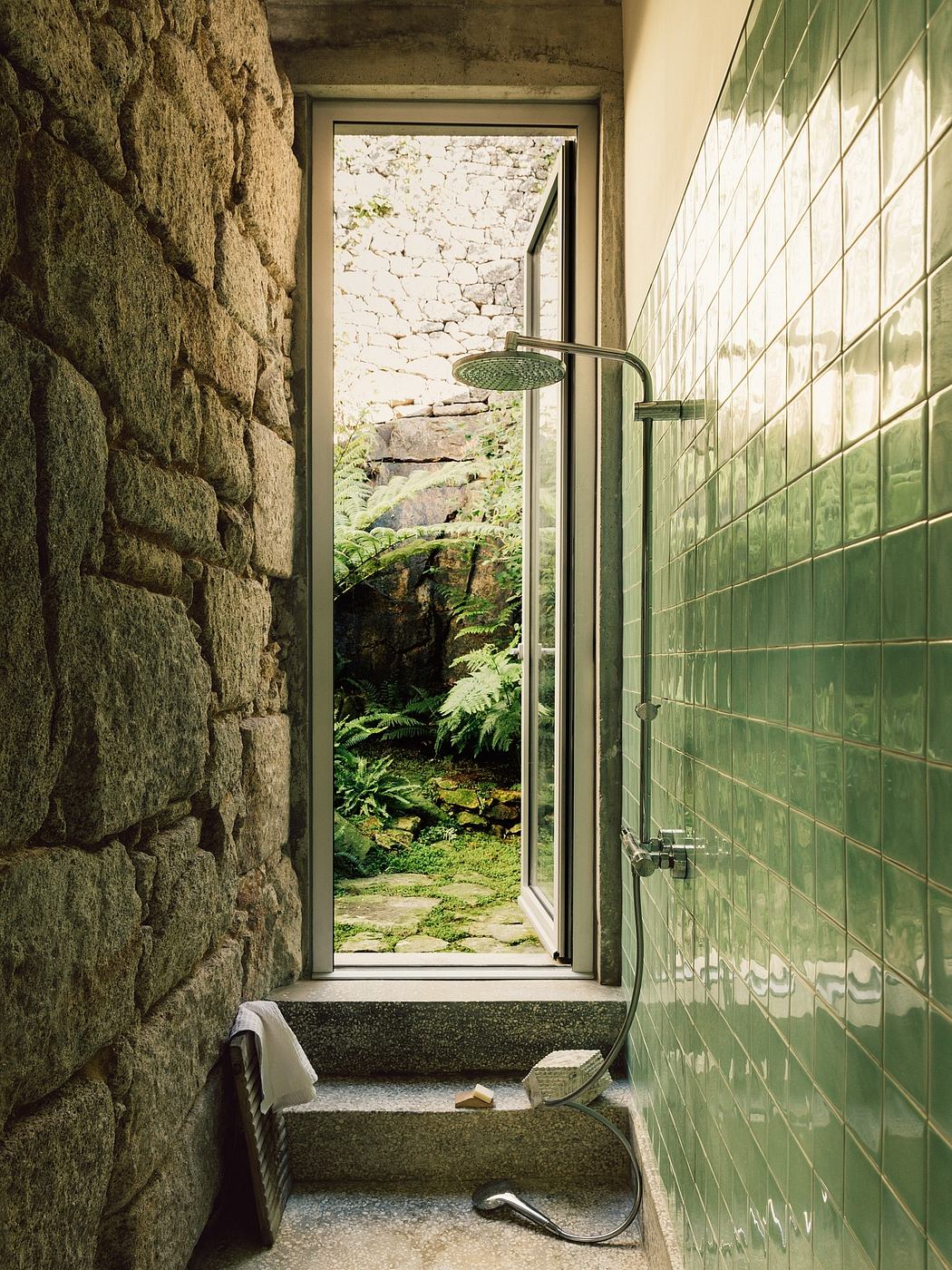 A serene, moss-covered stone shower nook with a lush forest view beyond, creating a tranquil retreat.