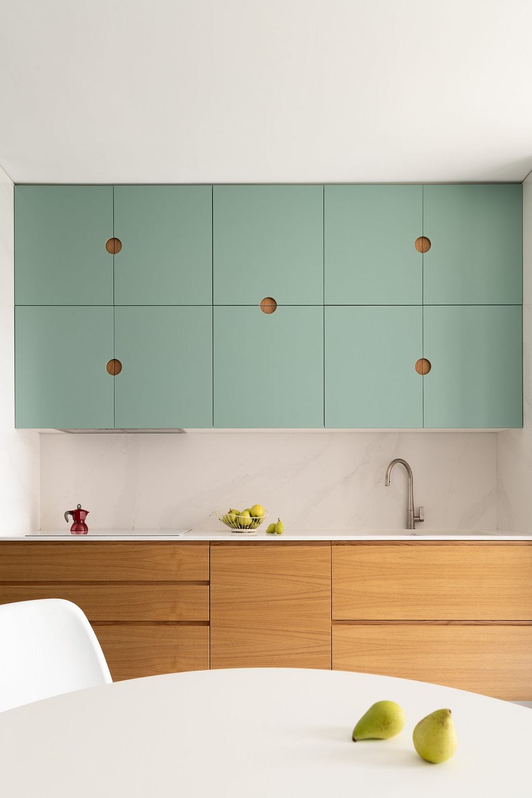 A modern kitchen with mint-colored cabinets, wooden drawers, and minimalist fixtures.