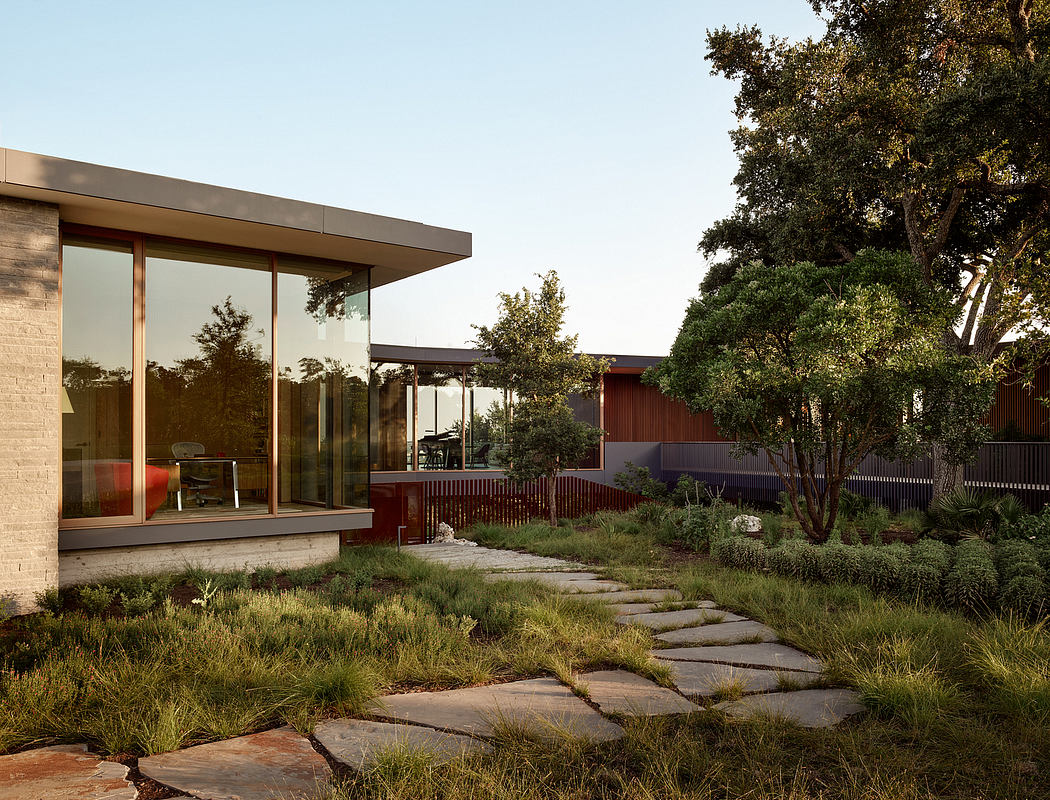 A modern glass-walled home nestled among lush foliage, with a stone path leading through the garden.