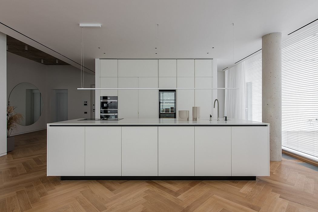 Spacious modern kitchen with minimalist white cabinetry, sleek appliances, and herringbone wood flooring.