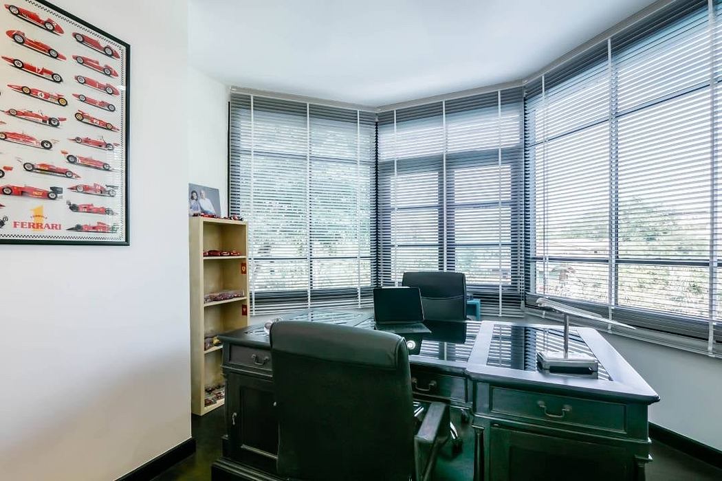 Sleek, minimalist office with expansive windows, framed Ferrari artwork, and modern furnishings.