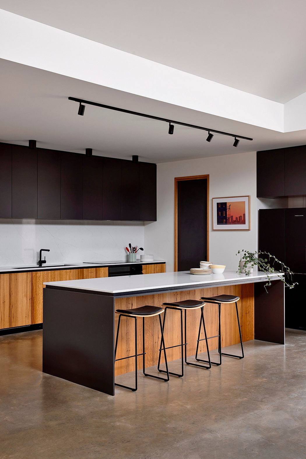 A modern kitchen with black cabinetry, wood accents, and sleek bar stools.