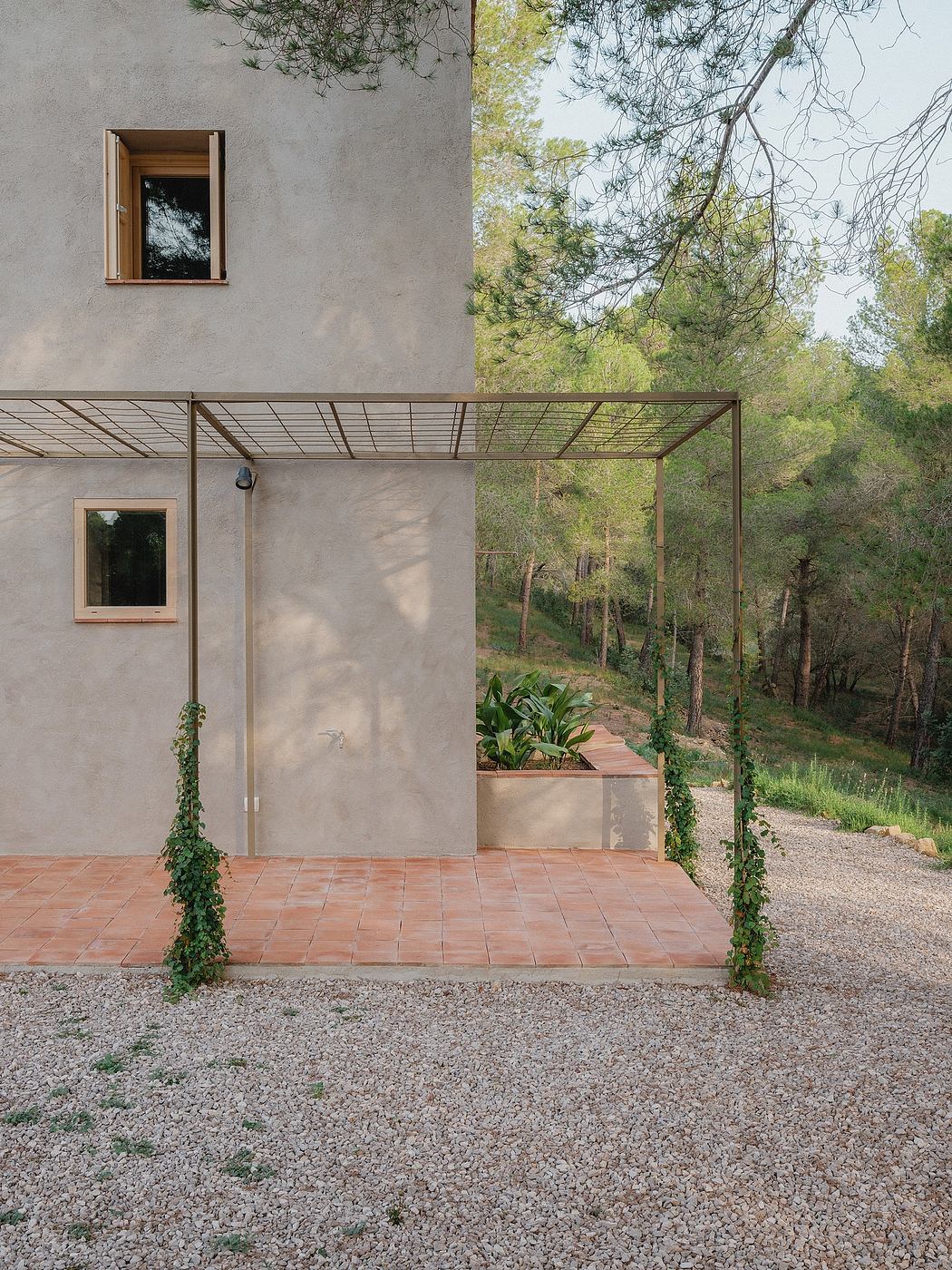 Gray concrete exterior with metal-framed porch and tiled terrace overlooking wooded landscape.