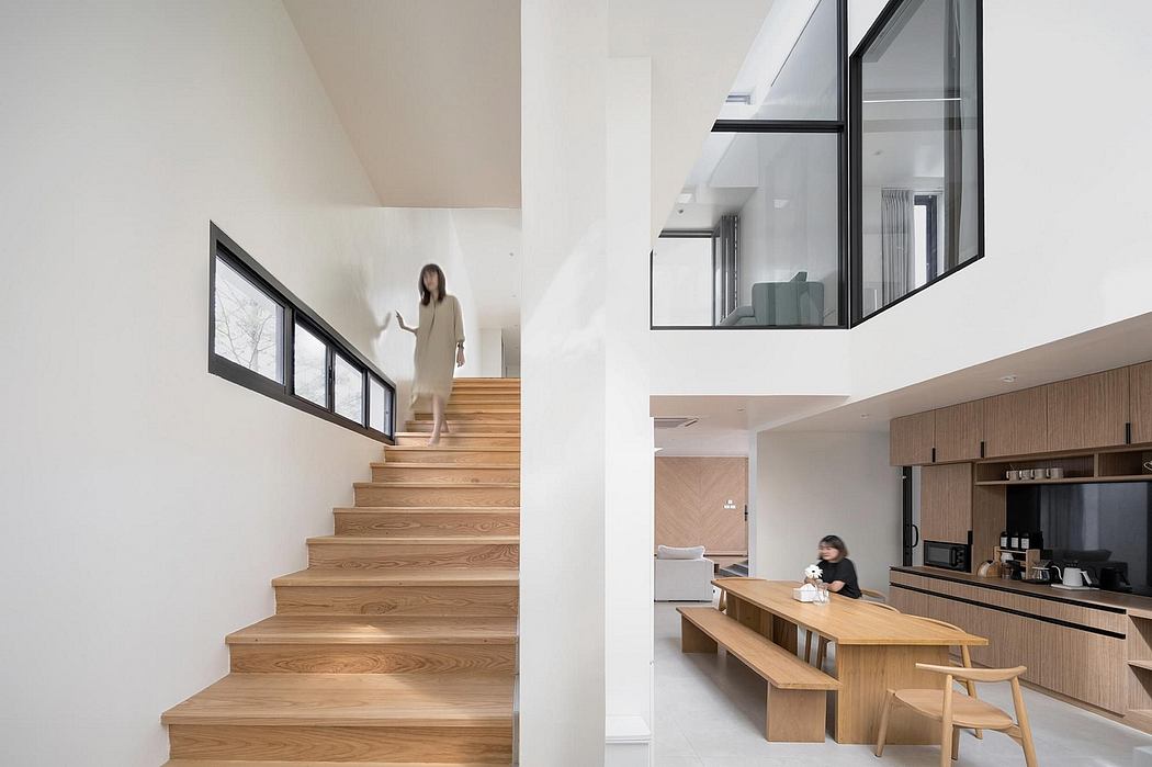 A modern, minimalist interior featuring wooden stairs, large windows, and an open kitchen.