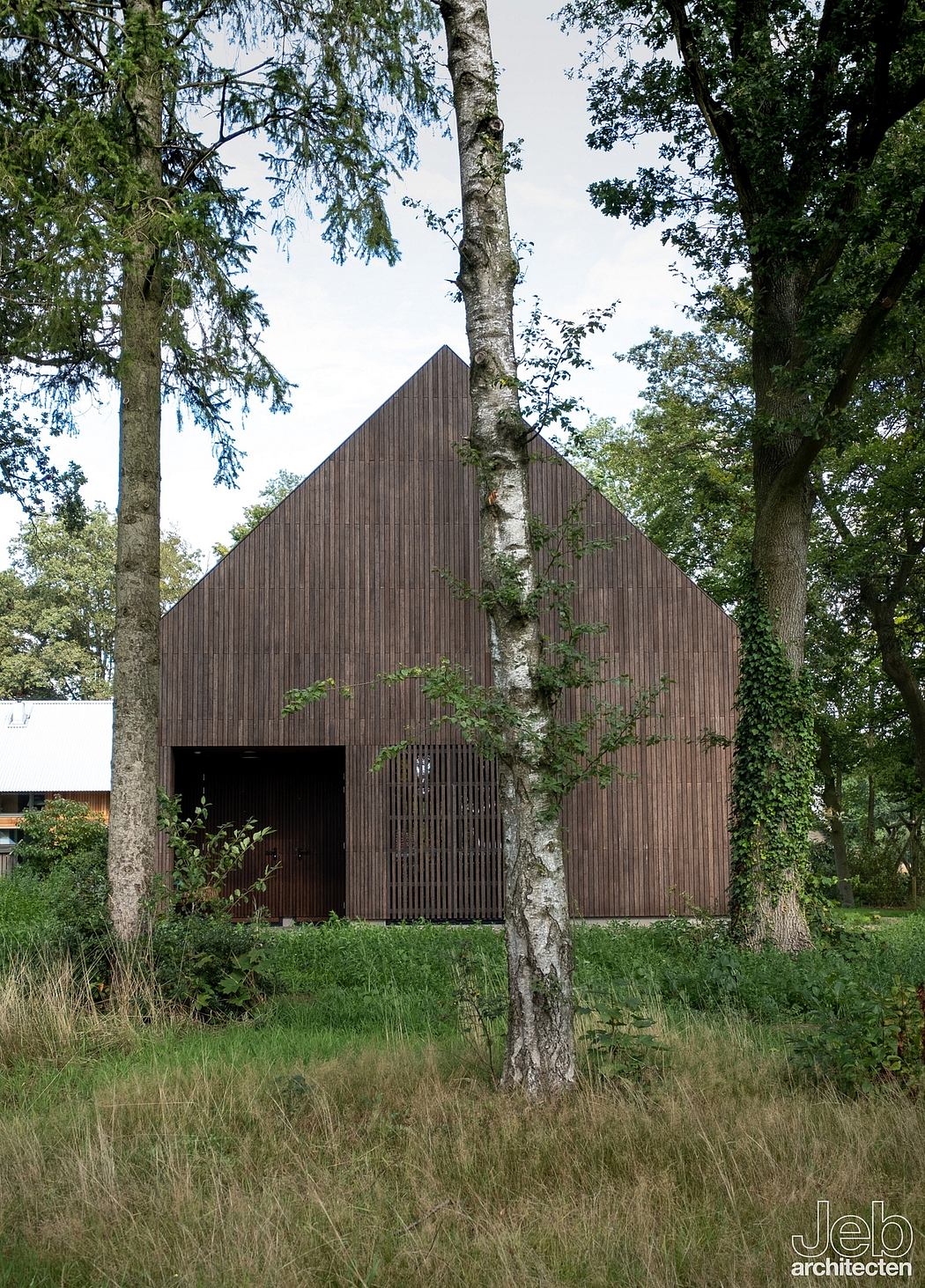 A wooden barn-like structure stands amidst lush greenery, highlighting its architectural design.