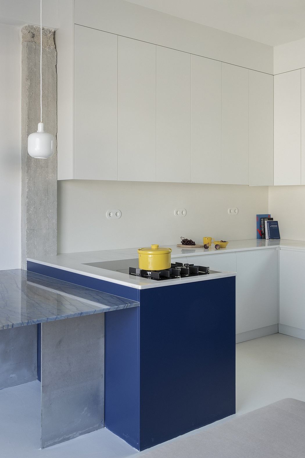 A minimalist kitchen with sleek cabinets, contrasting blue countertop, and concrete accents.