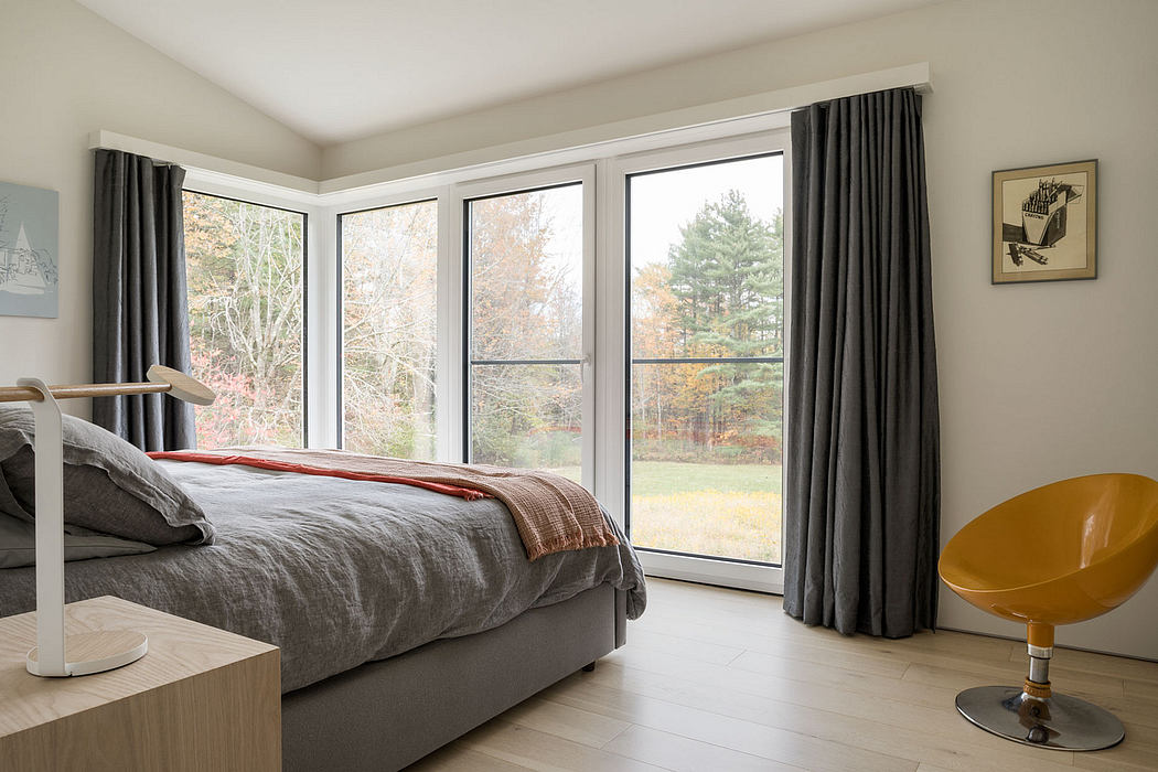 A spacious bedroom with floor-to-ceiling windows, neutral-toned furnishings, and a panoramic forest view.