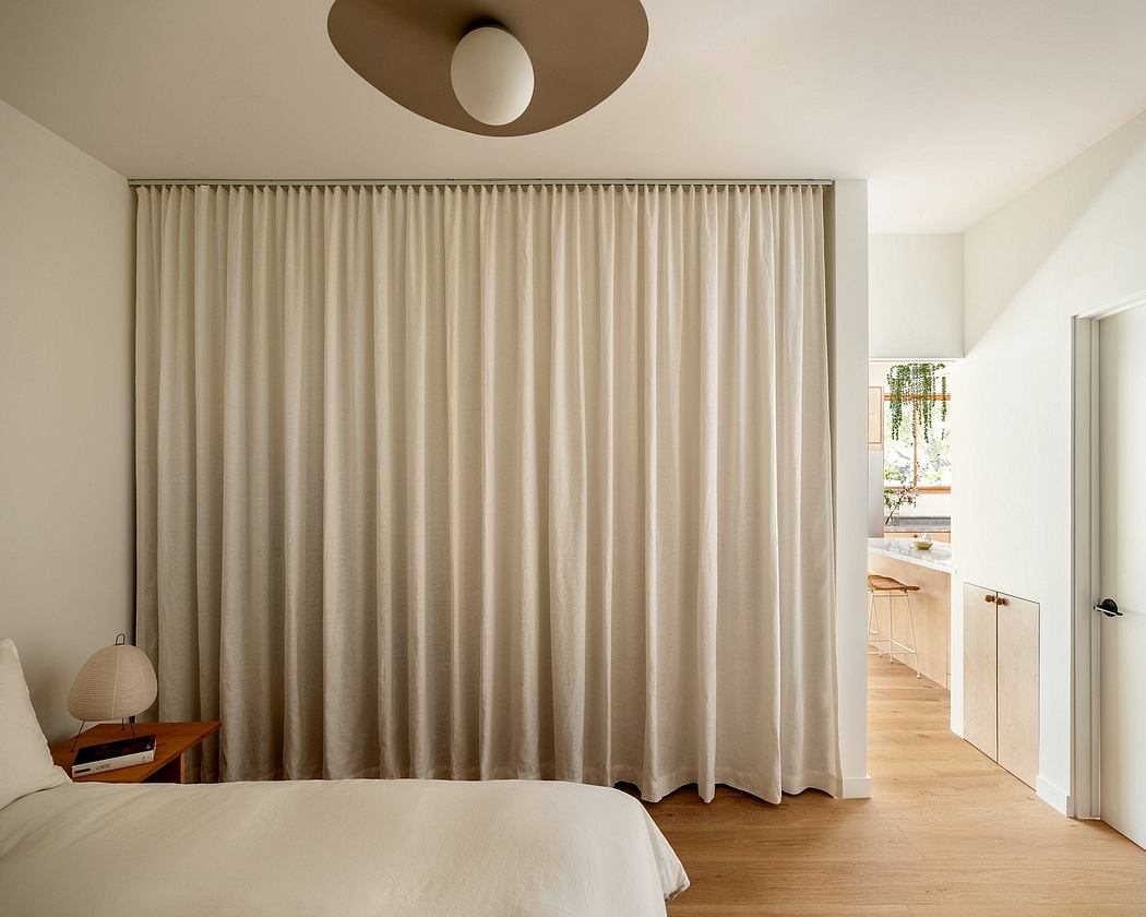 Cozy bedroom interior with neutral-toned curtains, wooden flooring, and modern lighting fixture.