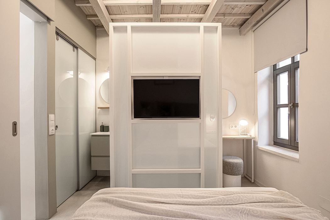 Clean, modern bedroom interior with built-in shelving and TV wall mount. Wooden ceiling beams.