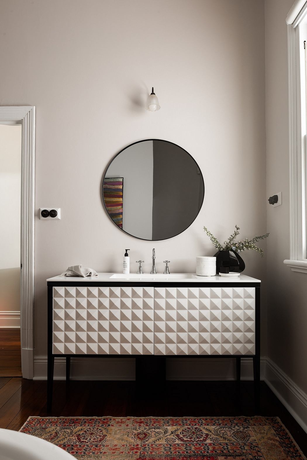 Sleek vanity with textured drawers, round mirror, and ornate rug contrast.