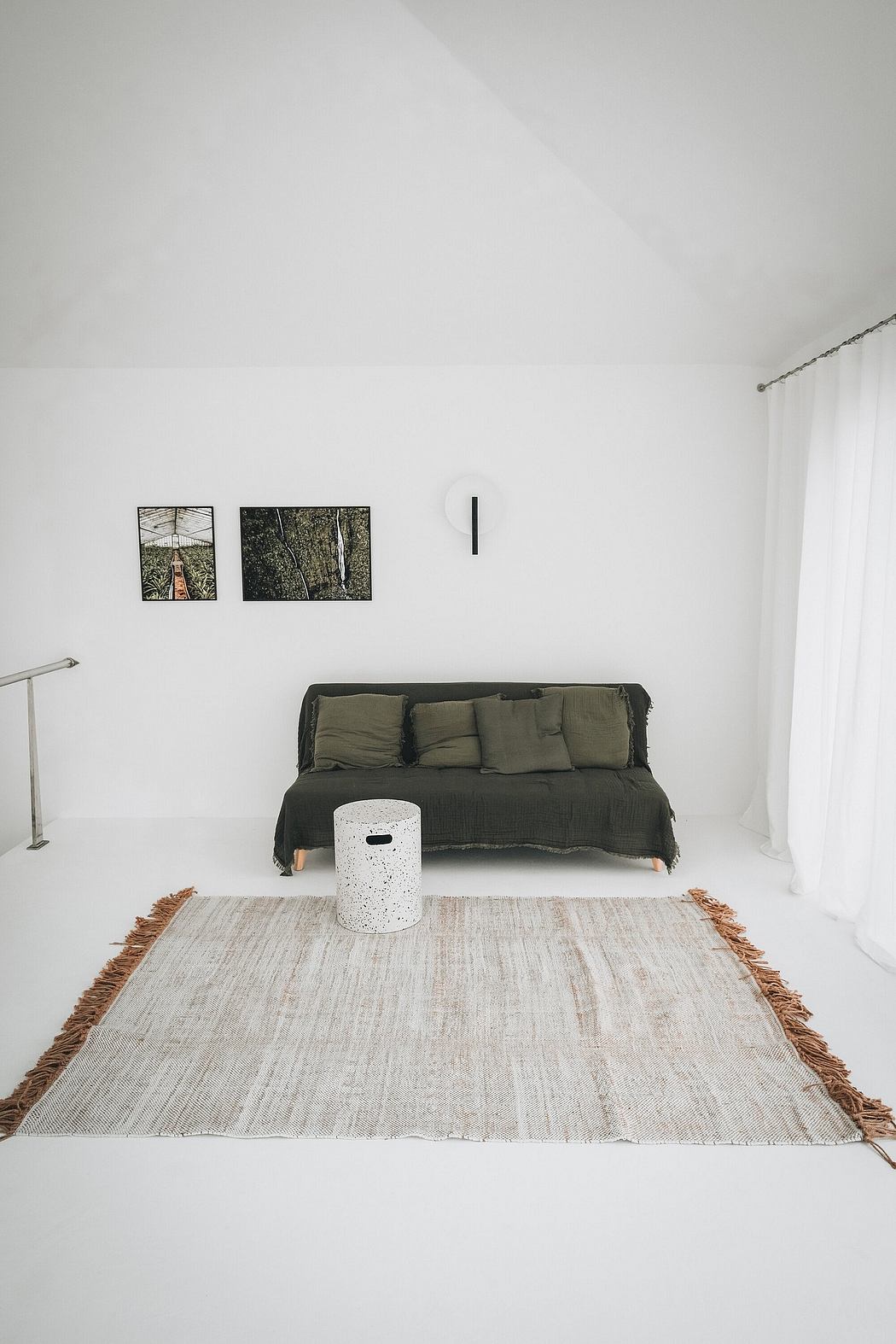 A minimalist living room with a dark green sofa, framed artwork, and a white area rug.